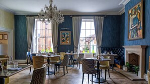 A dining area with multiple tables and chairs, a chandelier, and a fireplace. - Harbour Hotel Chichester (Chichester)