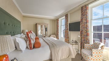 Un cuarto de hotel con una cama grande, un cabecero tapizado en verde, una mesita de noche con lámpara, una silla y vista a la ciudad a través de la ventana.