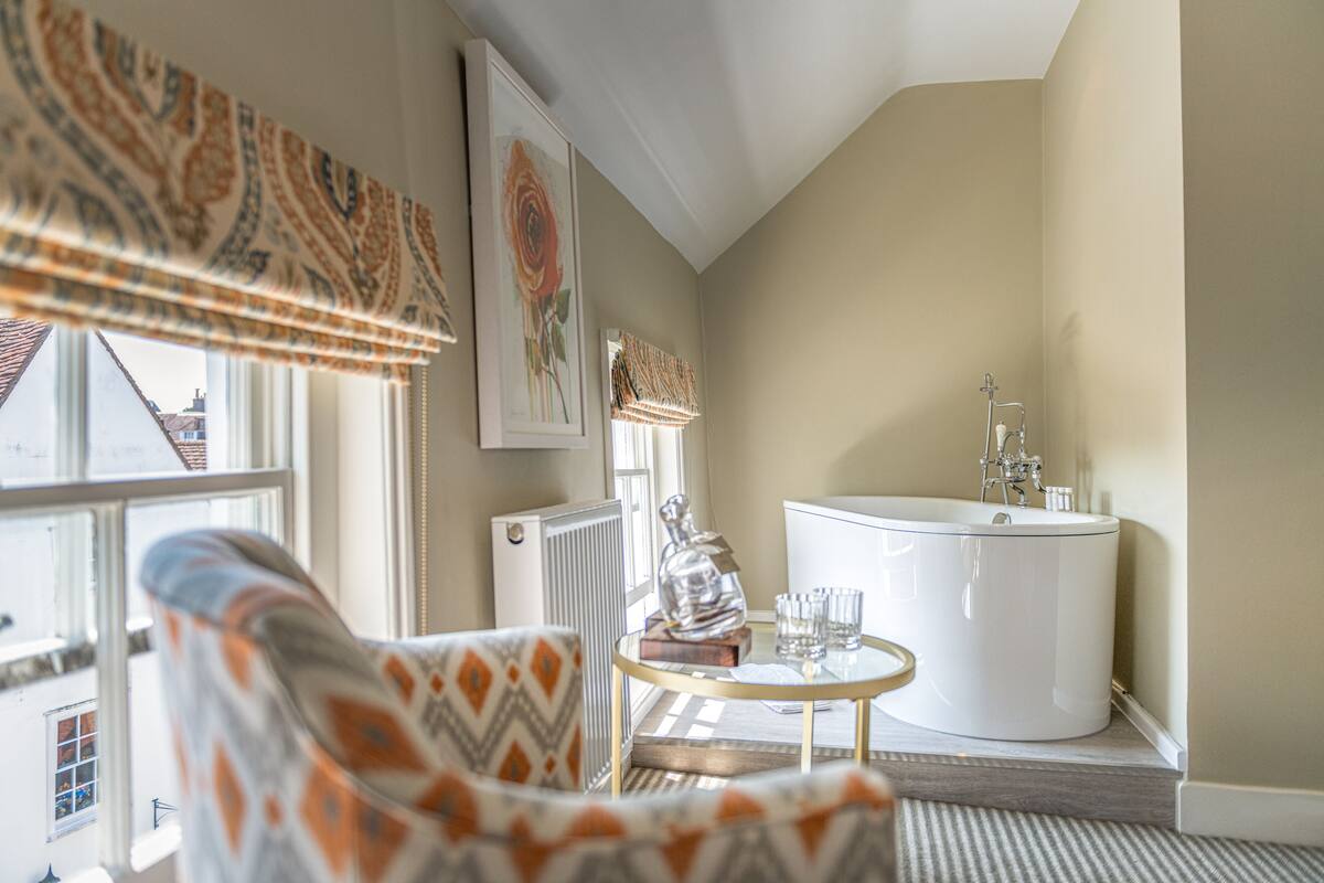A bathroom with a bathtub, a radiator, and a window with curtains.
