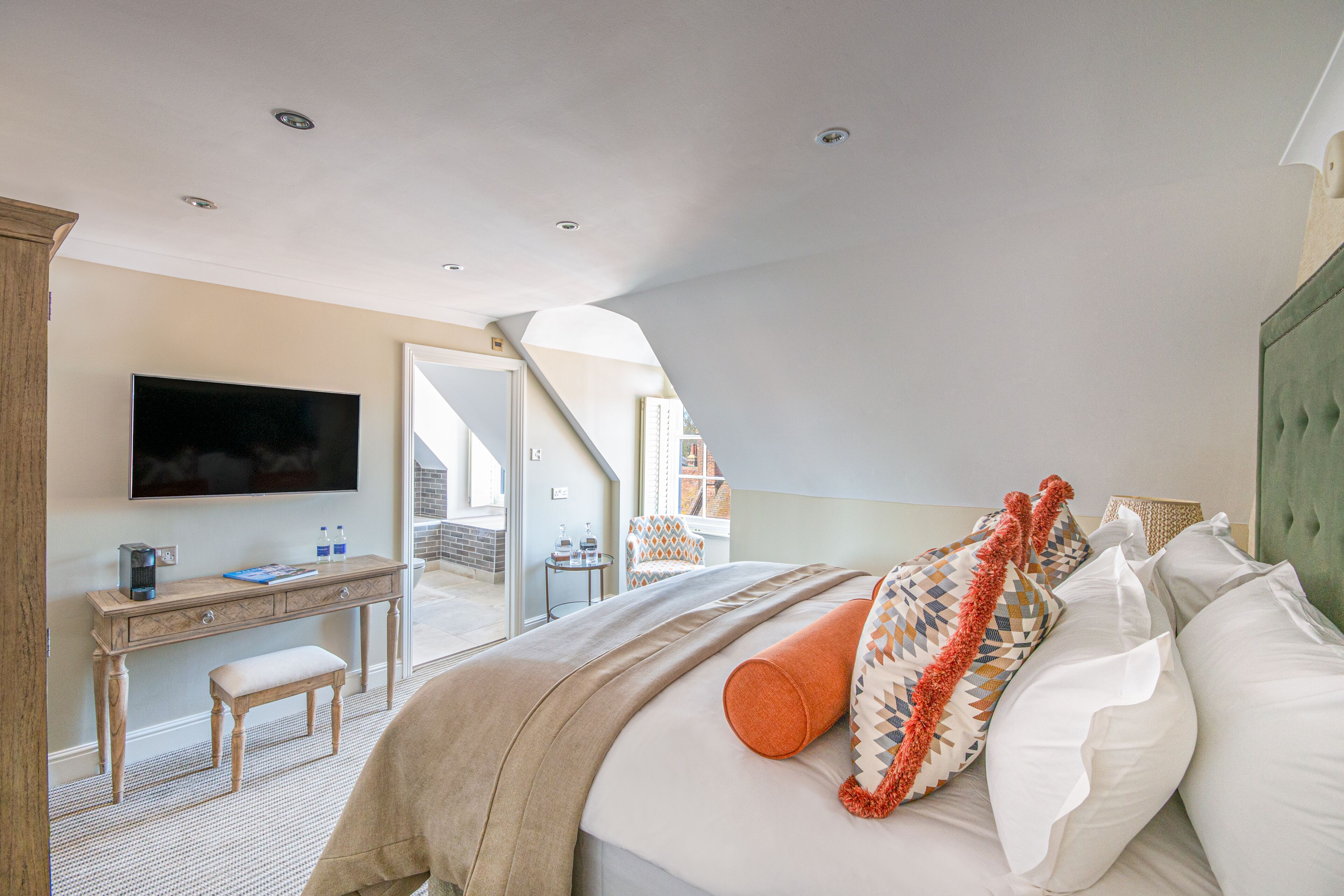 A bedroom with a bed, pillows, a desk, a chair, and a television.