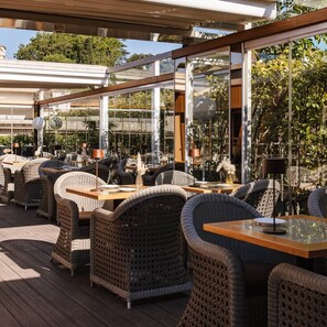 Ein Sitzbereich im Freien mit Korbmöbeln und Glastischen, umgeben von einer Holzterrasse und Glasgeländern.