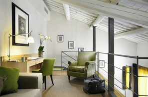 Ein Hotelzimmer mit Schreibtisch, zwei Stühlen, einem Bett, einer Treppe und einem Geländer.