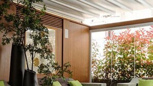 Un área de estar al aire libre moderna con mobiliario de mimbre, cojines verdes y plantas en macetas.