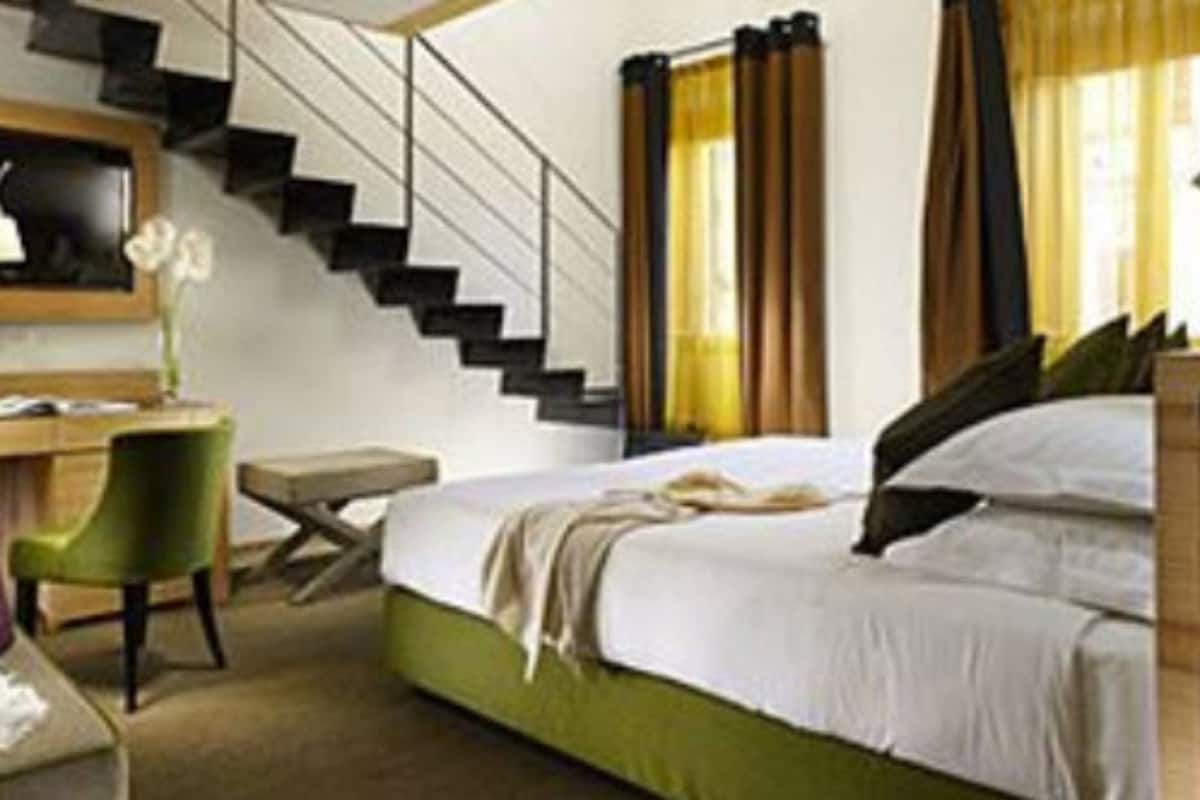 Habitación de hotel con cama, escritorio, silla, escalera y ventana con cortinas.