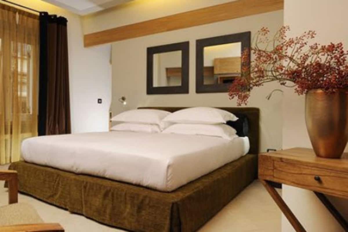 Habitación de hotel con una cama grande, cabecera de madera, mesita de noche, un florero con flores y un espejo en la pared.