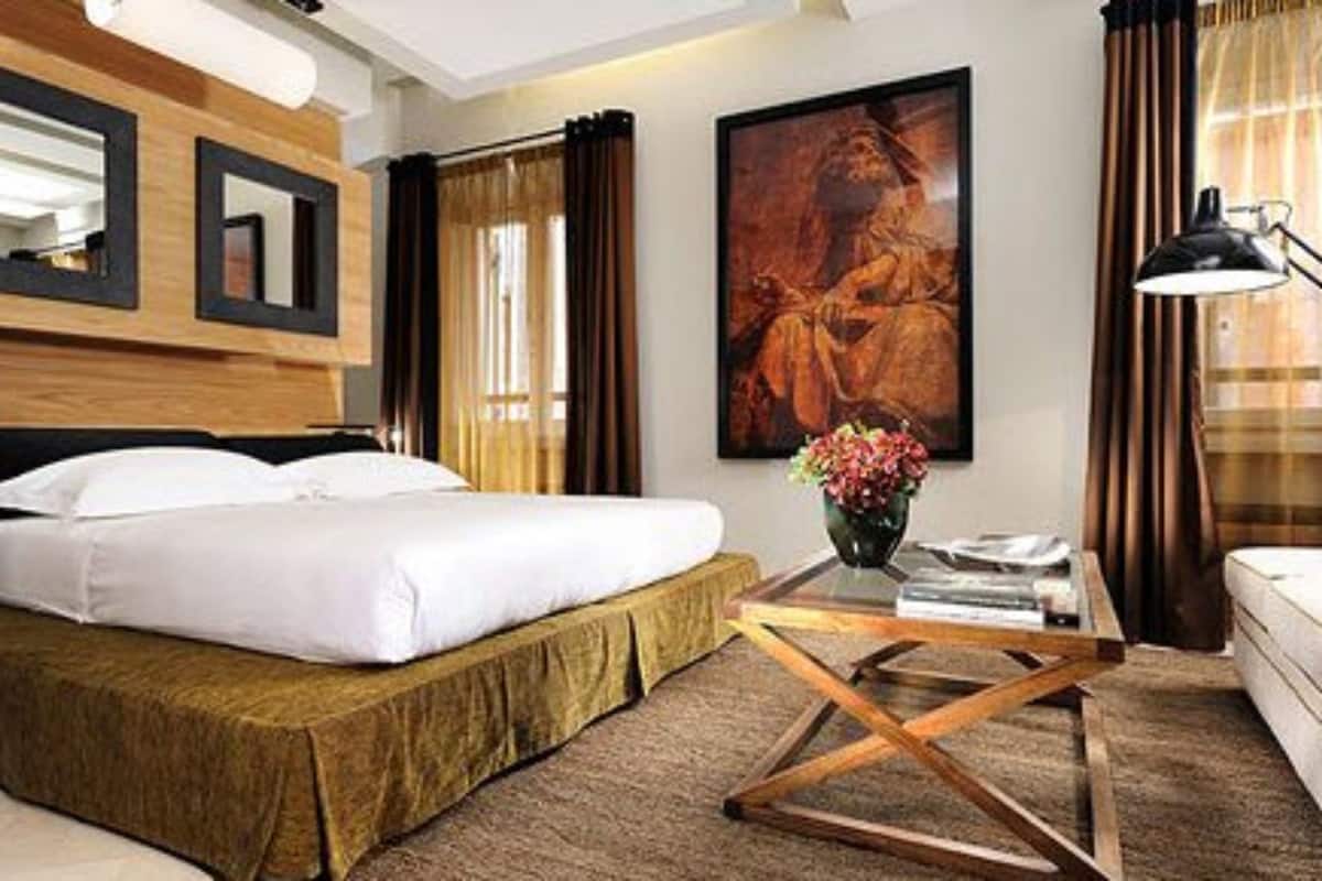 Habitación de hotel con cama, escritorio, silla, lámpara, un cuadro y cortinas.