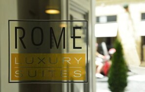 A sign for "ROME LUXURY SUITES" with a clear glass window. - Babuino 181 – Small Luxury Hotels of the World (Rome)