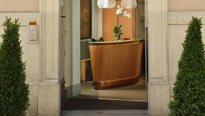Entrada de hotel con diseño clásico, que incluye un amplio mostrador de recepción de madera y dos plantas en macetas.