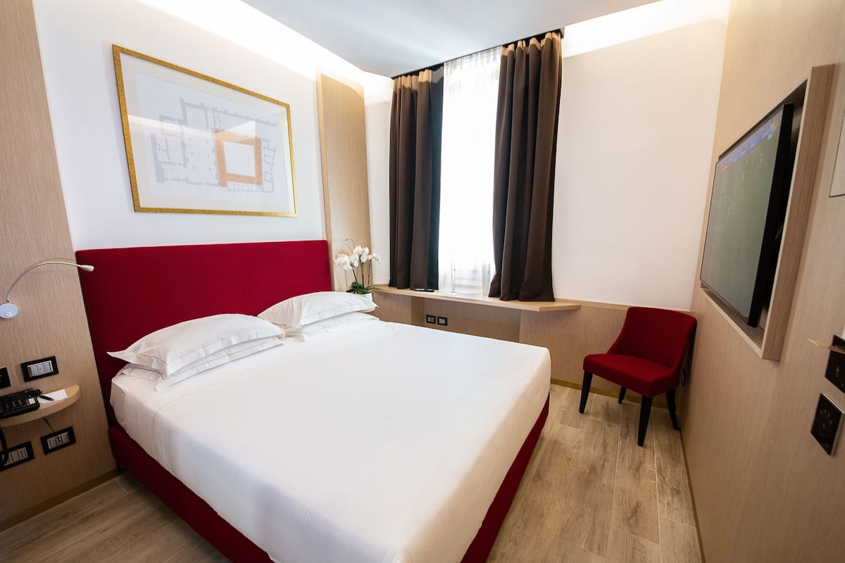 Habitación de hotel con una cama grande, un escritorio con silla, un televisor y una ventana con cortinas.
