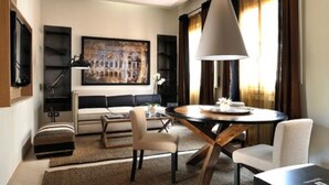 Una sala de estar moderna con un sofá, una mesa de centro y sillas, una mesa de comedor con una lámpara, y un cuadro grande en la pared.