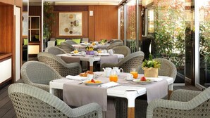 Un coin petit-déjeuner aménagé avec des meubles en osier, des tables dressées avec des assiettes, des tasses et un panier de fruits.