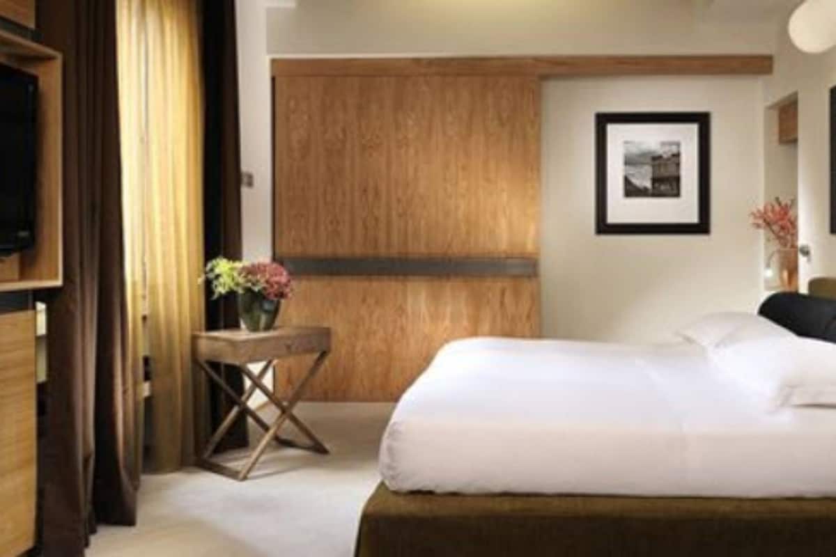 Una habitación de hotel con una cama, un armario de madera, una mesita con un florero y un cuadro en la pared.