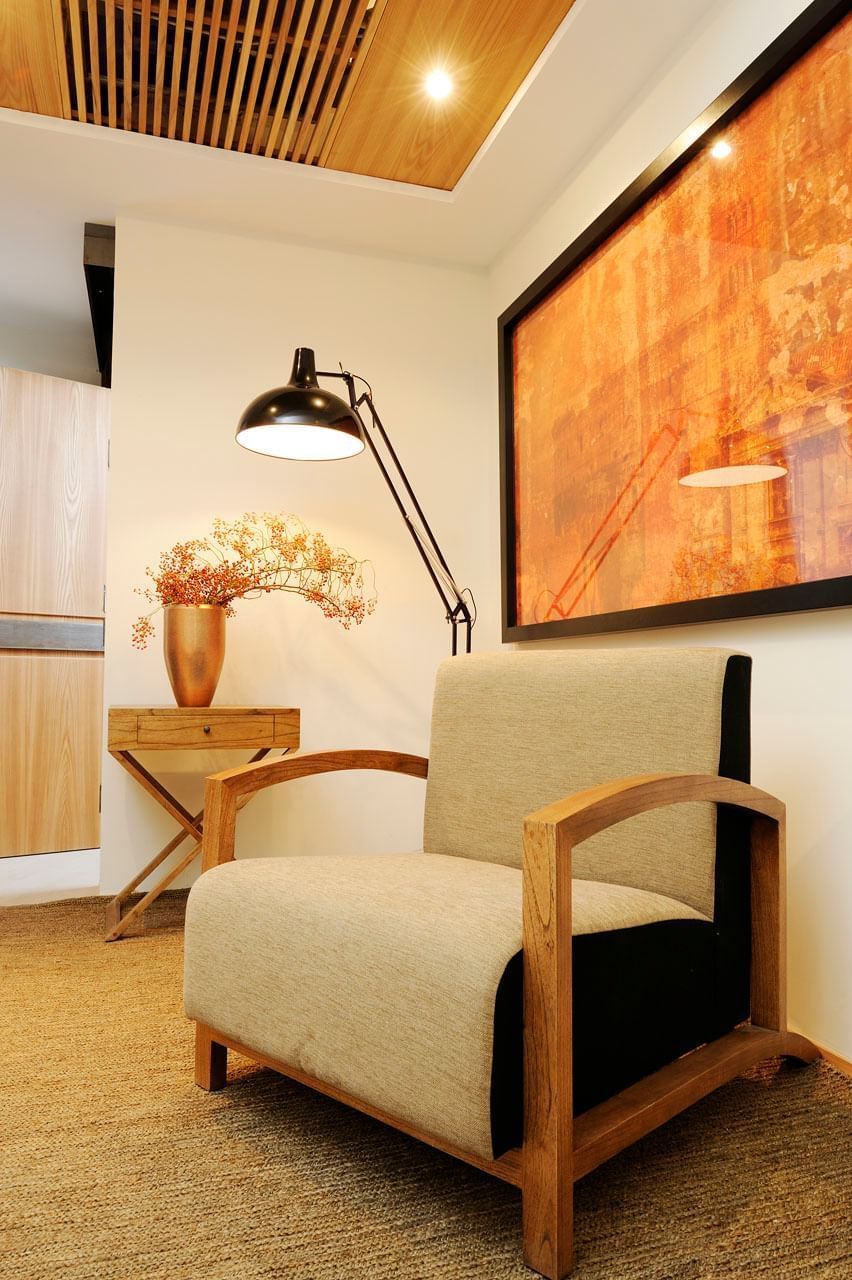 A modern room with a wooden chair, a desk with a lamp, and a large abstract painting on the wall.