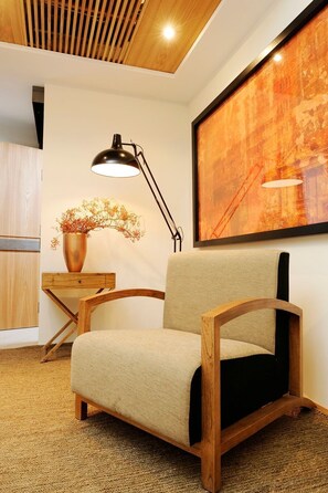Ein modernes Zimmer mit einem Holzstuhl, einem Schreibtisch mit Lampe und einem großen abstrakten Gemälde an der Wand.