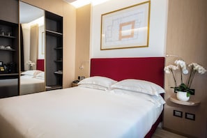 A hotel room with a large bed, a red headboard, a mirror, a nightstand, a wall-mounted plant, and a framed architectural drawing. - Babuino 181 – Small Luxury Hotels of the World (Rome)