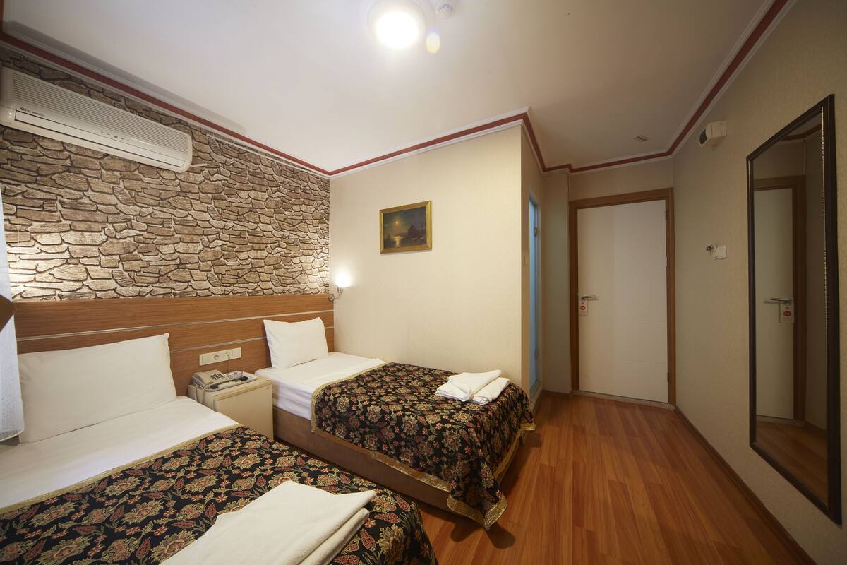 A hotel room with two beds, a stone wall, a painting, and a wooden floor.