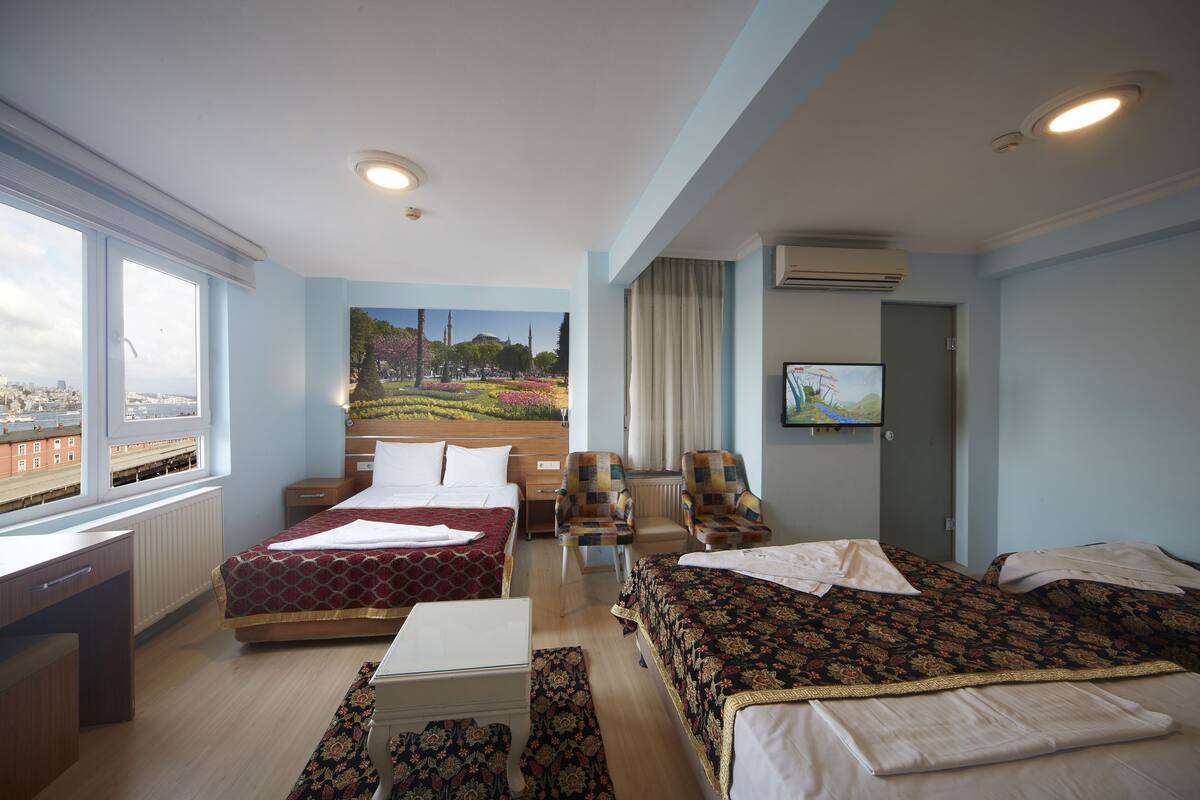 A hotel room with two beds, a desk, a chair, a TV, and a window with a city view.