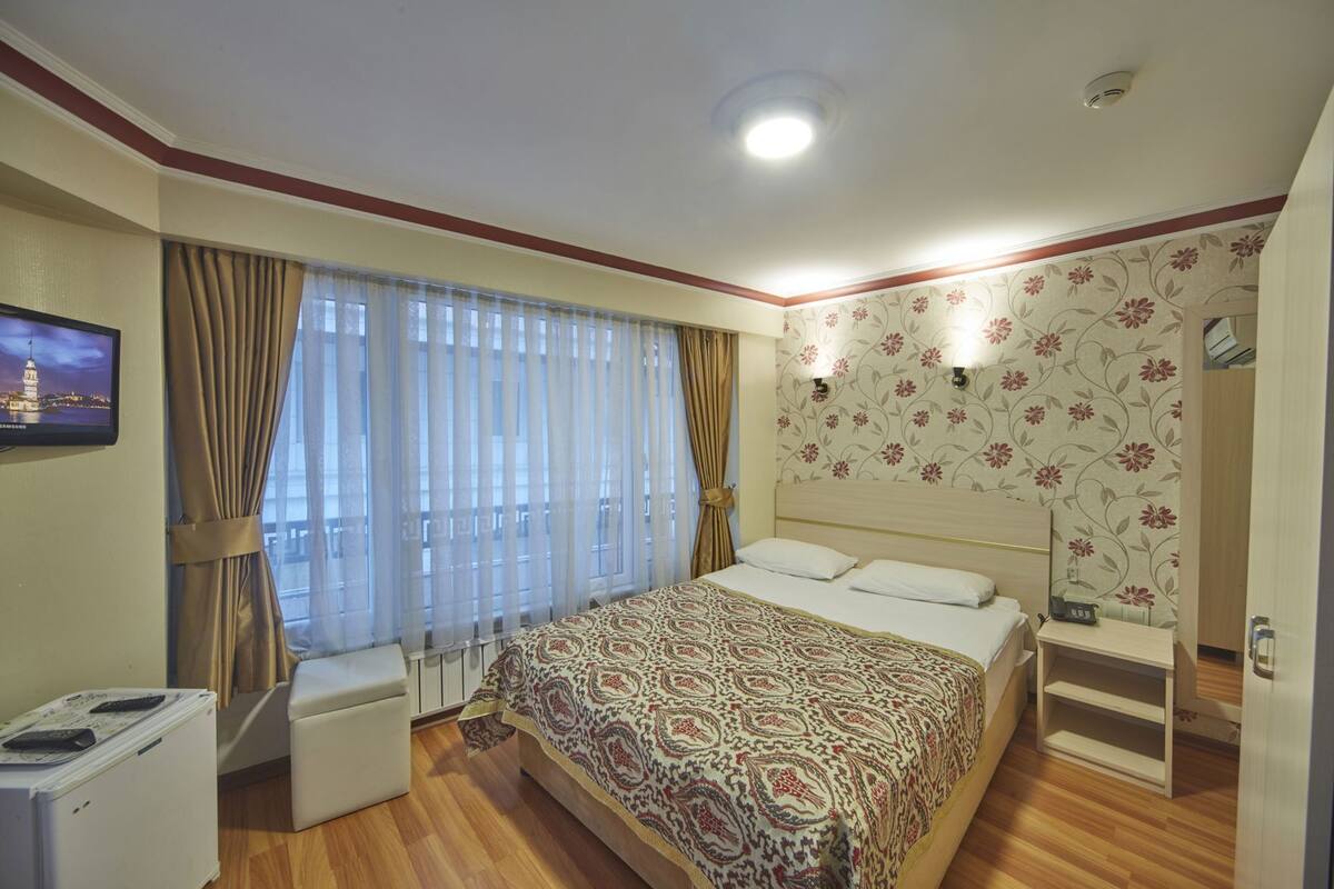 A hotel room with a bed, a television, a desk, a chair, and a wardrobe.