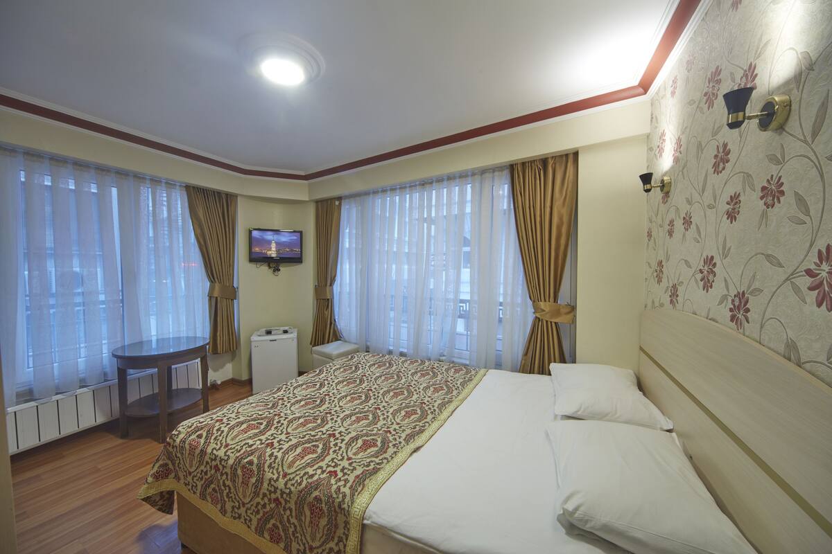 A hotel room with a large bed, a small table, a TV, and curtains.