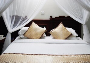Una cama con dosel, ropa de cama blanca y almohadas estampadas.