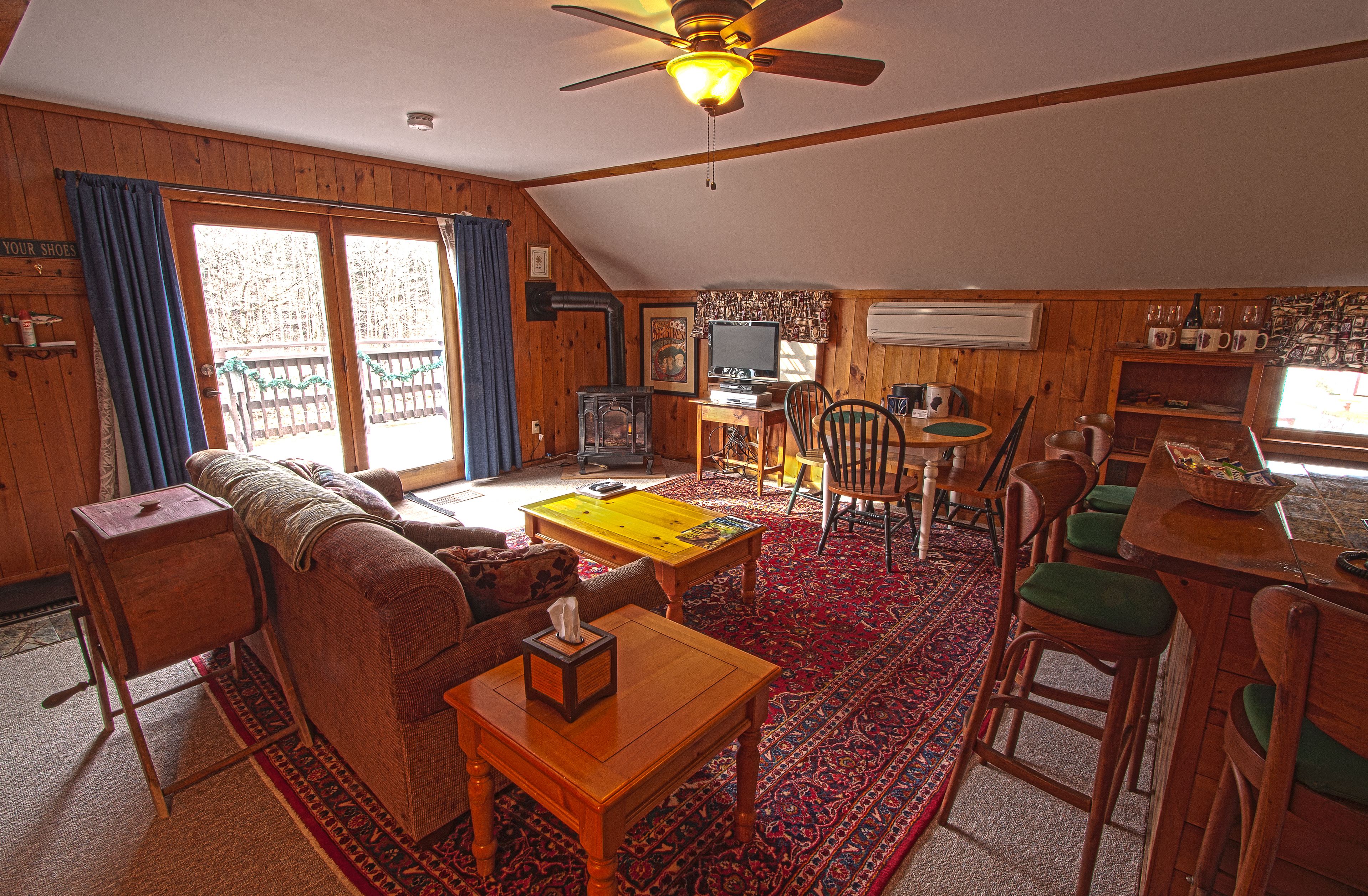 A cozy cabin-style room with a wooden interior, a sofa, a coffee table, a dining table with chairs, and a television.