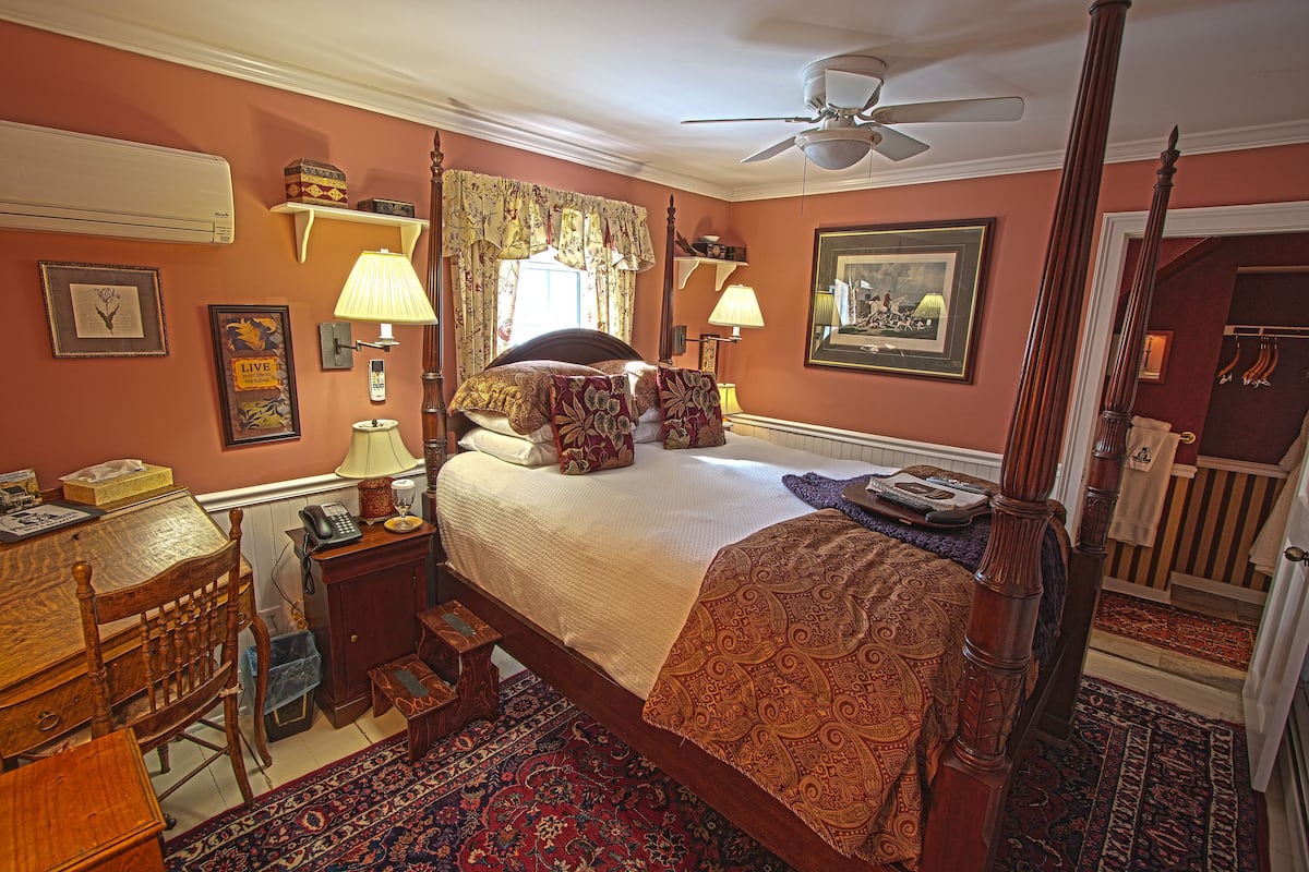 A traditional bedroom with a four-poster bed, a desk with a chair, a telephone, and a radiator.