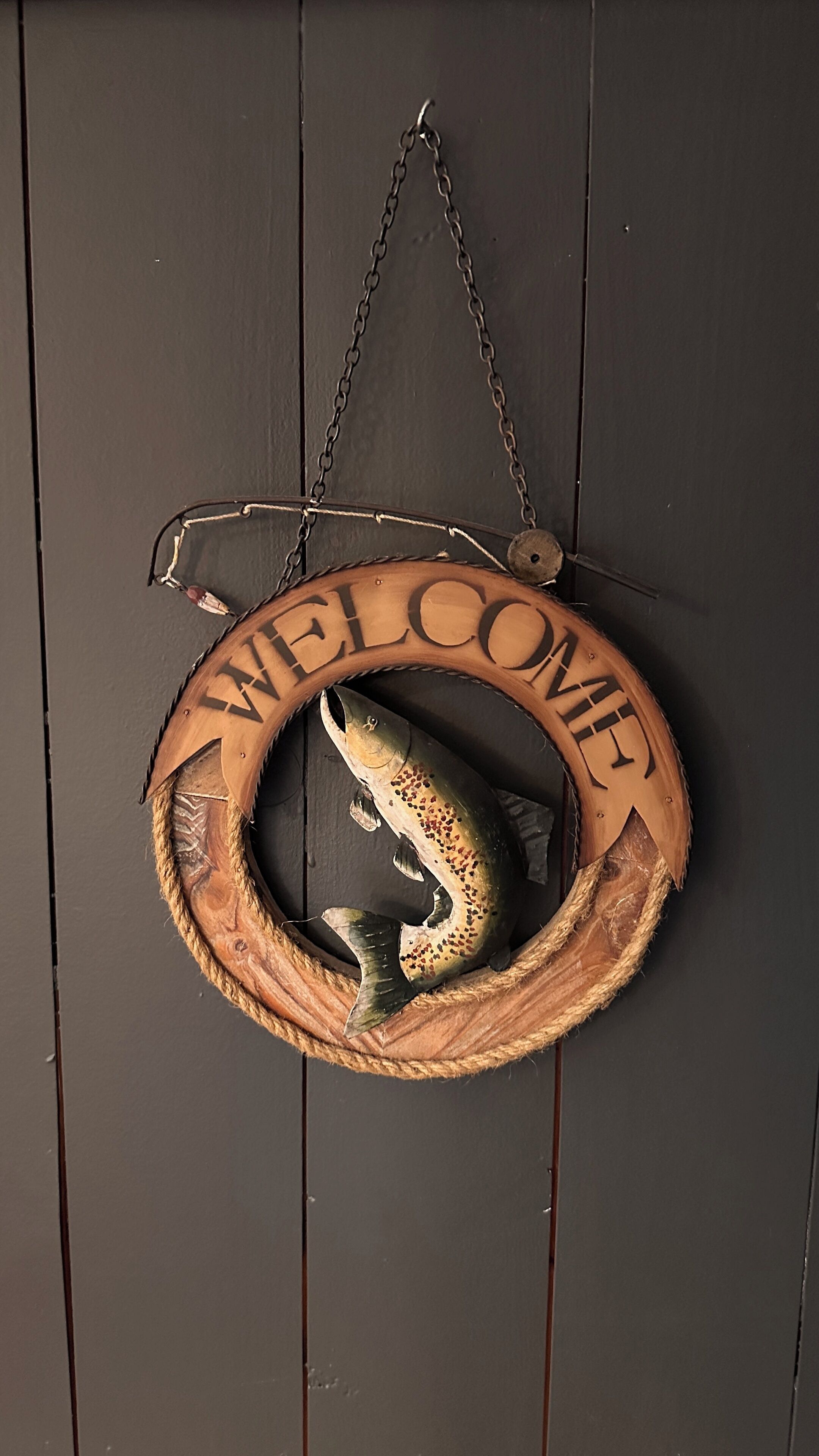 A wooden welcome sign with a fish design and the words "WELCOME" on a dark wooden door.