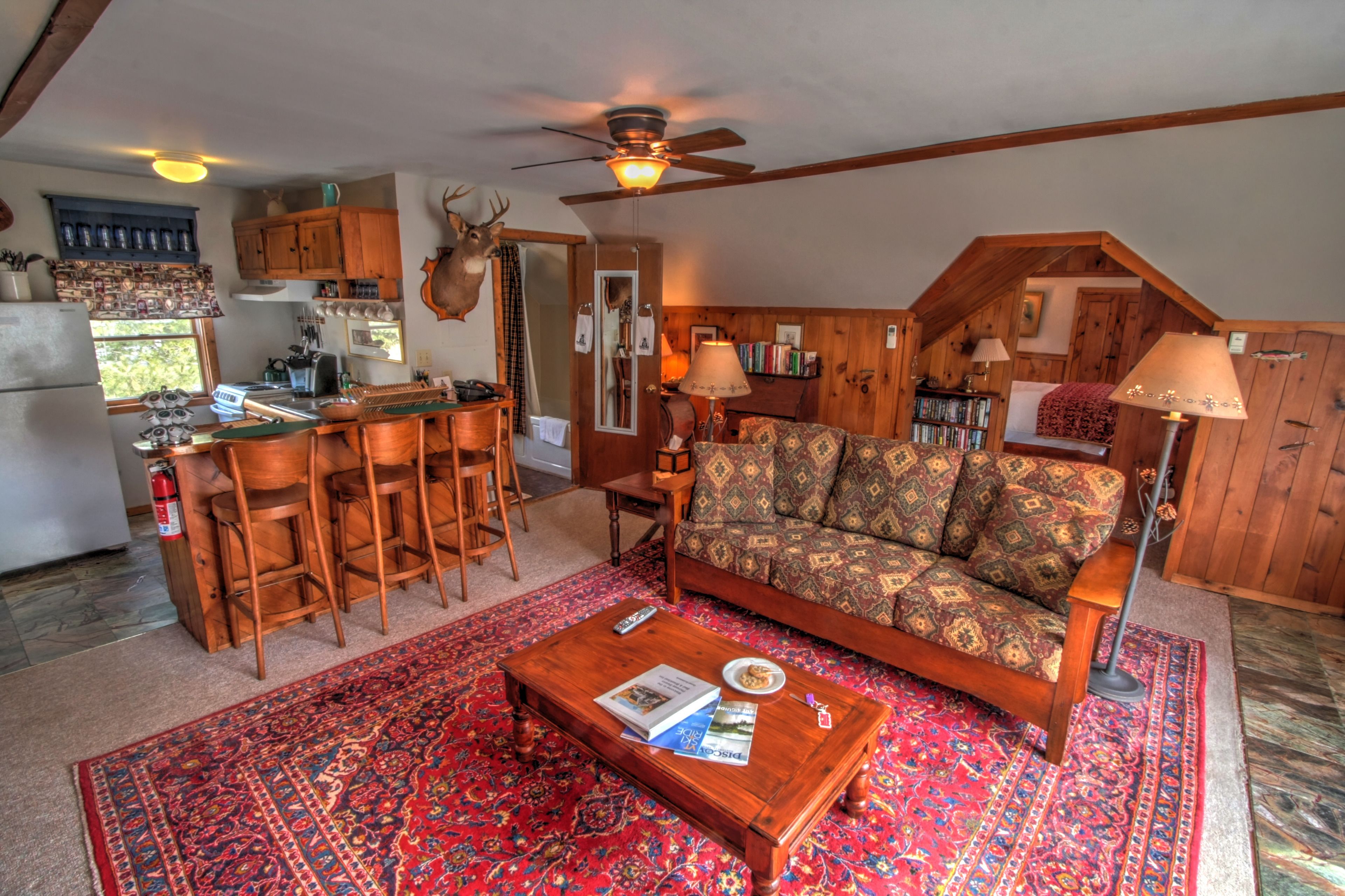A cozy living room with a patterned sofa, a coffee table with books, and a red rug.