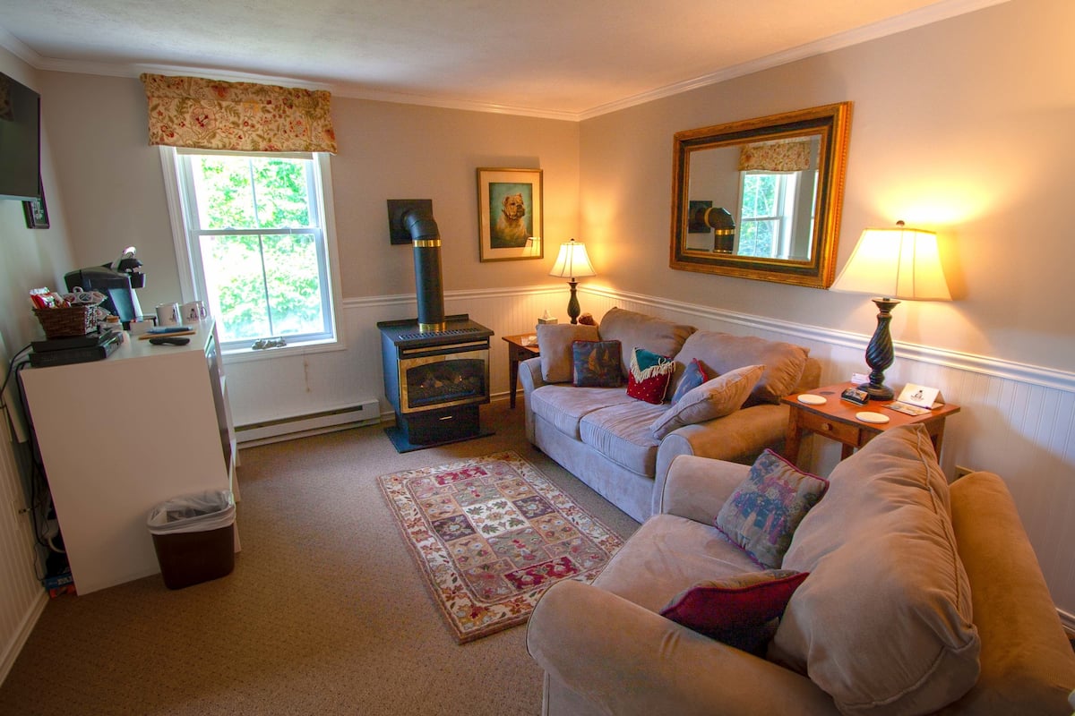 A cozy living room with a sofa, a fireplace, a lamp, and a window with curtains.