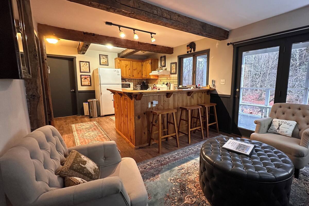 A cozy living room with a bar area, a large window with a view, and a fireplace.