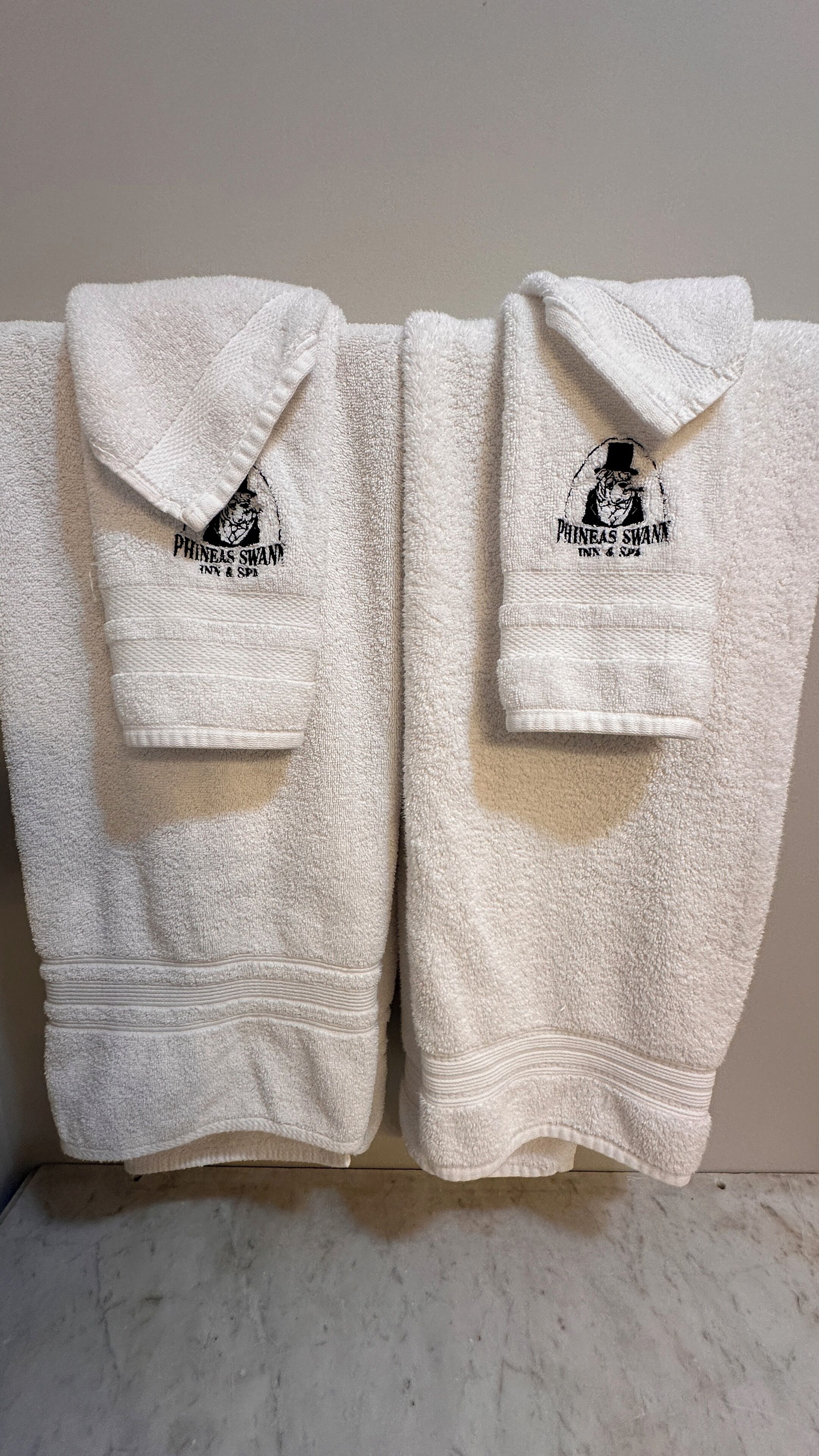 Two white towels with embroidered logos and text, hanging on a wall.
