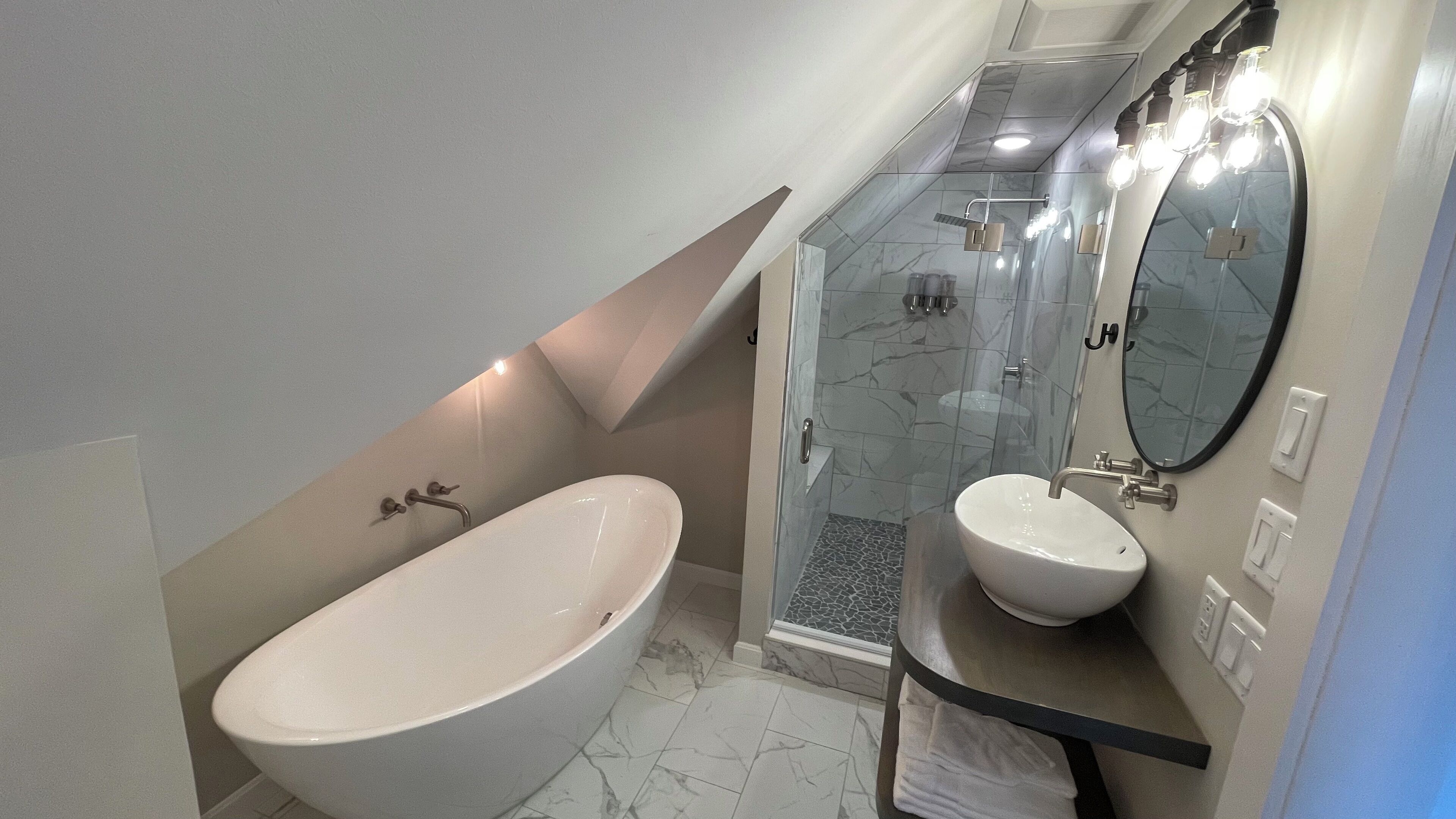 Een moderne badkamer met een vrijstaand bad, een wastafel met spiegel en een douche met glazen deuren.