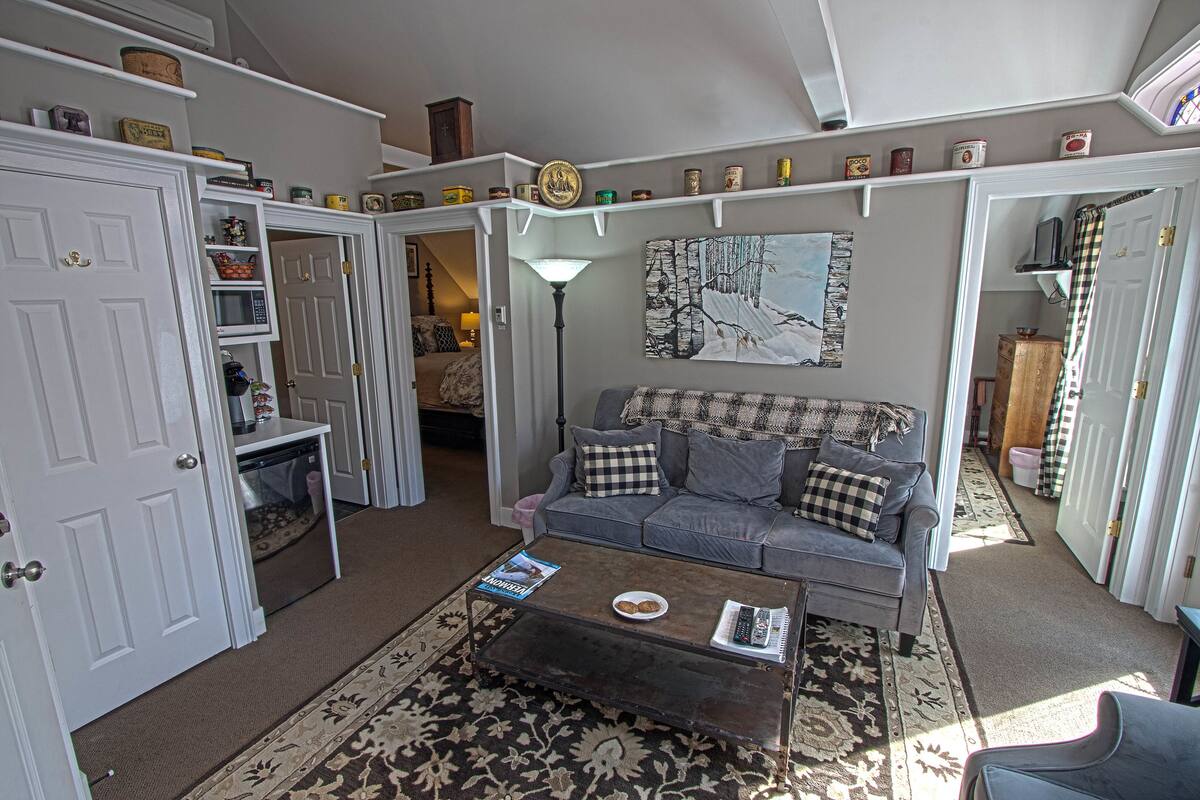 A cozy living room with a grey sofa, a coffee table with a magazine, and a patterned rug.