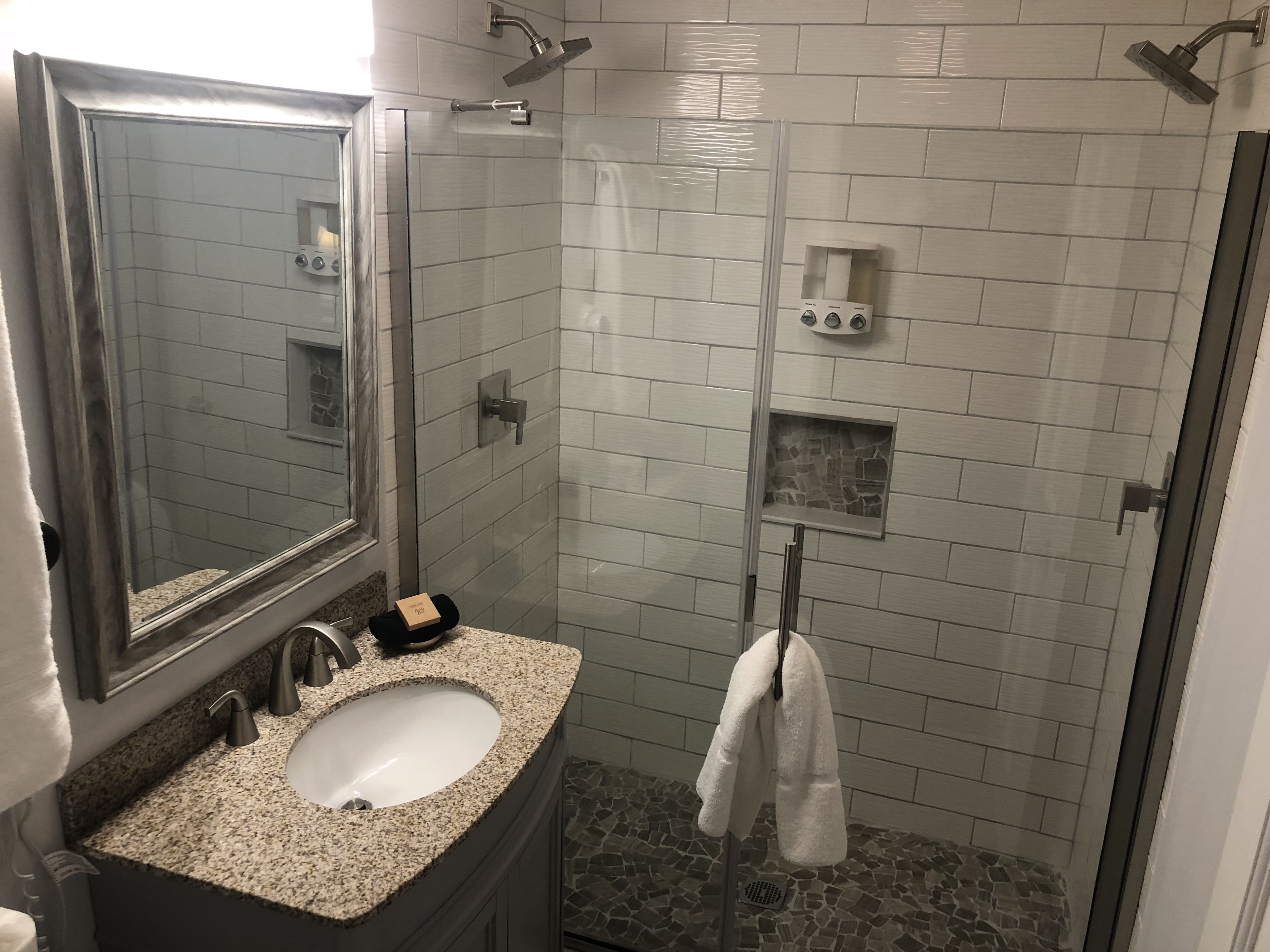 A bathroom with a granite countertop sink, a mirror, a glass-enclosed shower, and a towel rack.