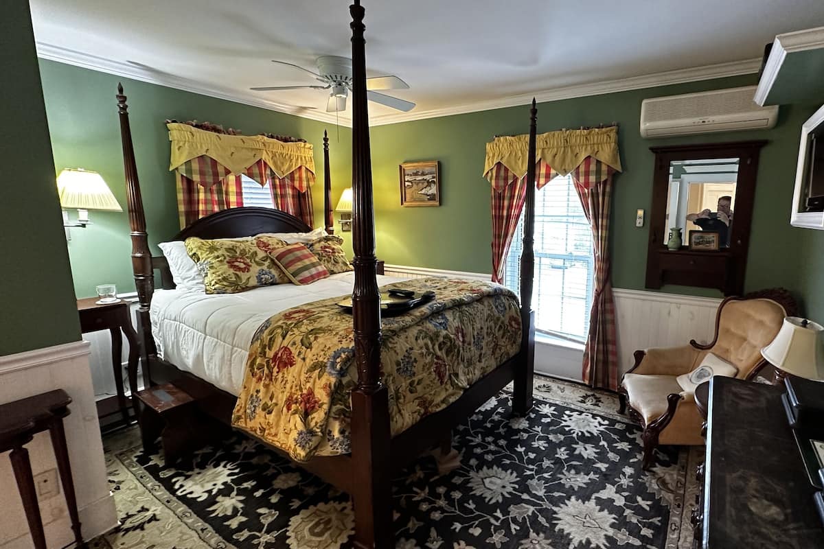 A four-poster bed with a floral bedspread, a standing lamp, and a mirror on the wall.