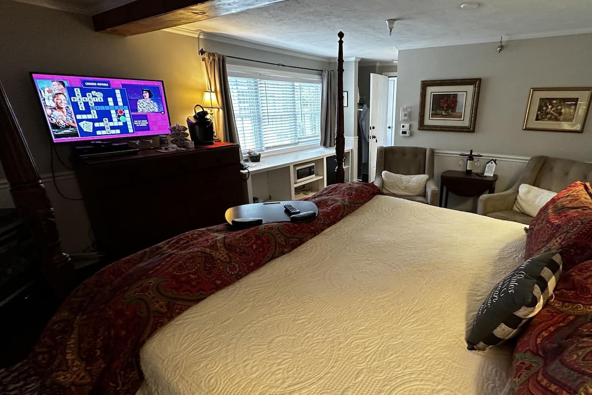 A hotel room with a large bed, a television displaying a game, a desk with a lamp, and a chair.
