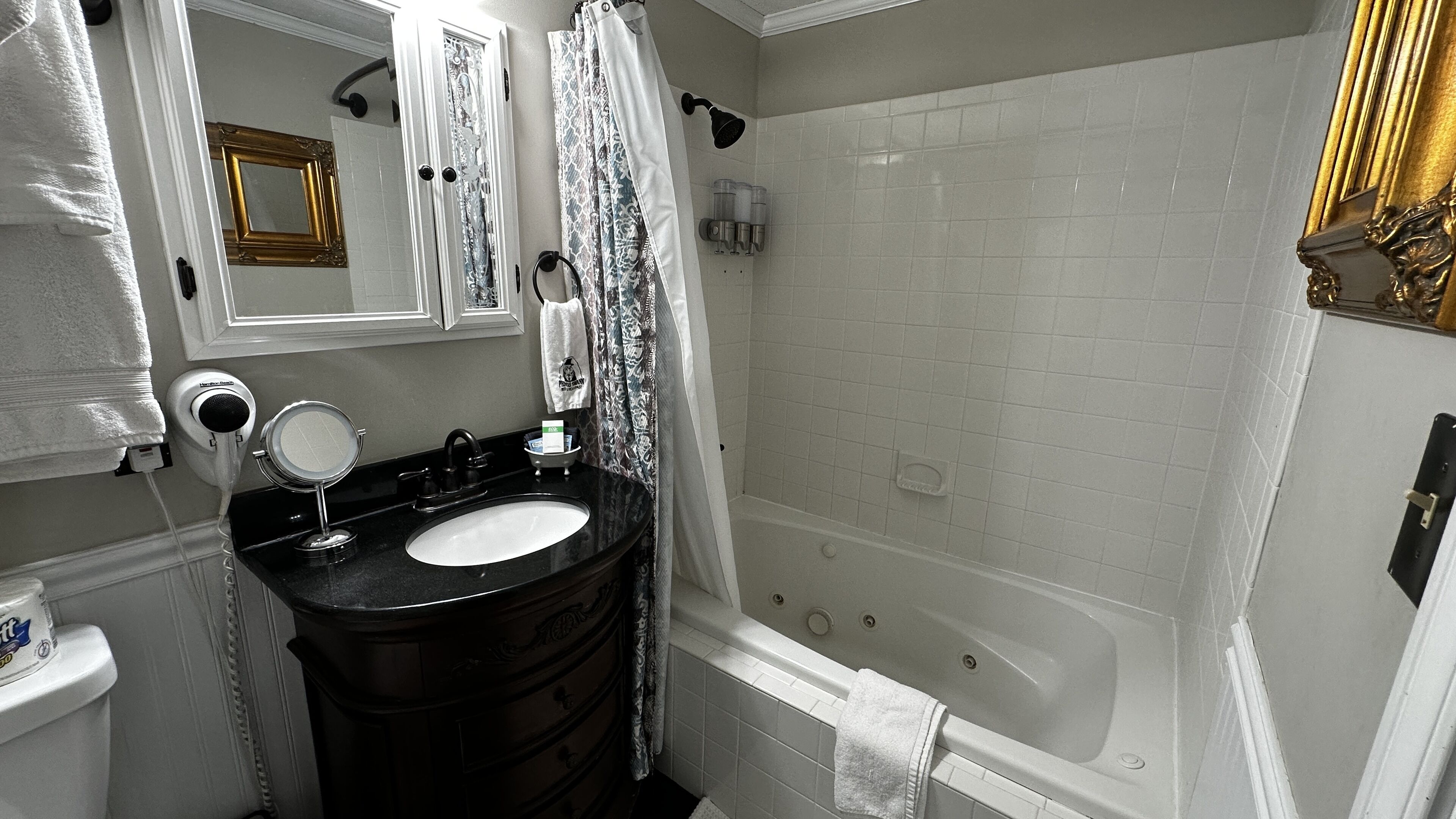 A bathroom with a black vanity, a white sink, a mirror, a shower, and a bathtub.