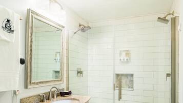 A bathroom with a white vanity, a sink, a mirror, and a glass-enclosed shower area.