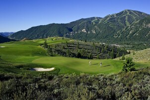 Un campo de golf con vistas panorámicas a montañas y un pueblo pequeño al fondo.