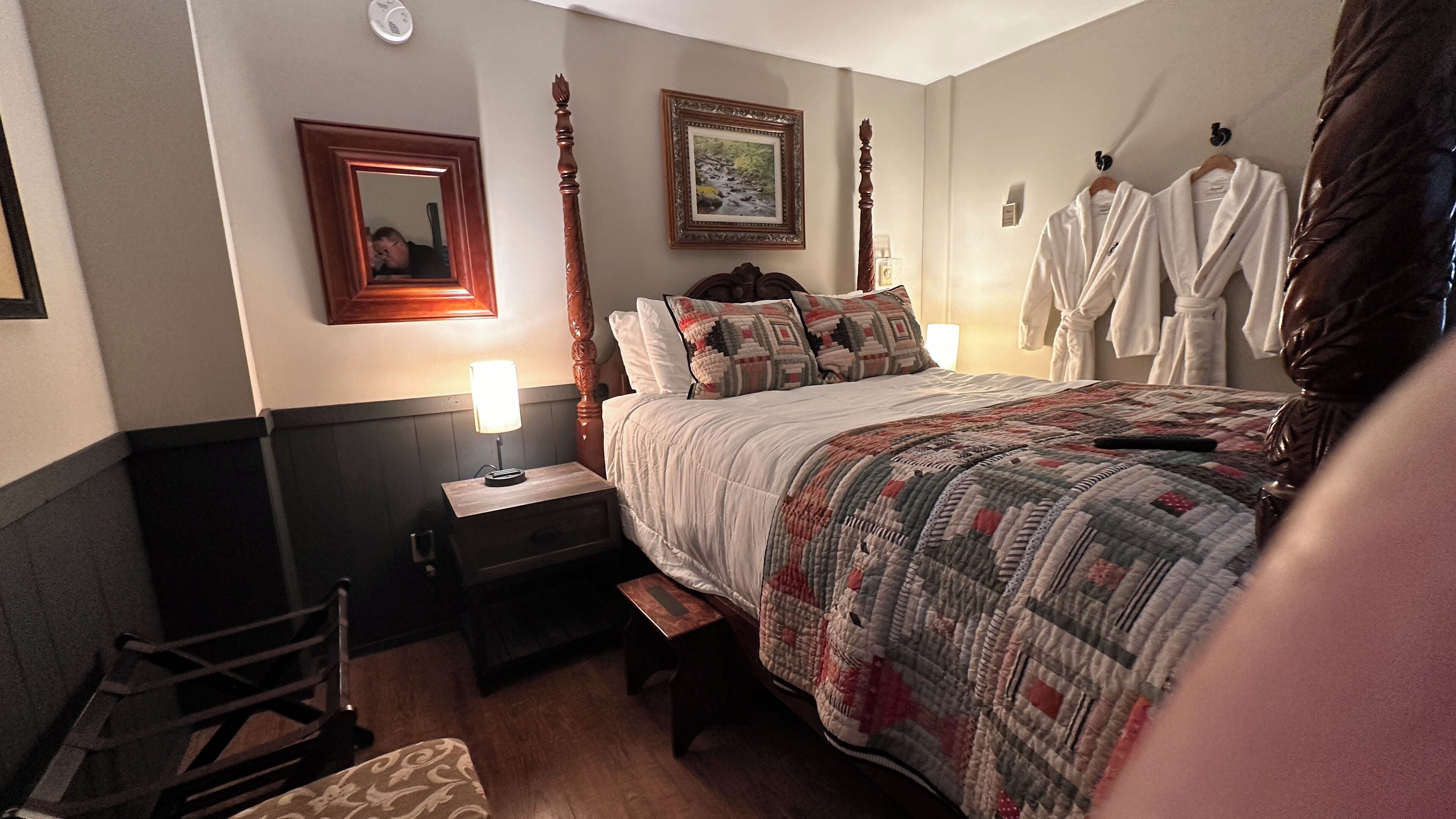 A bedroom with a bed, bedside table, lamp, mirror, and a picture on the wall.
