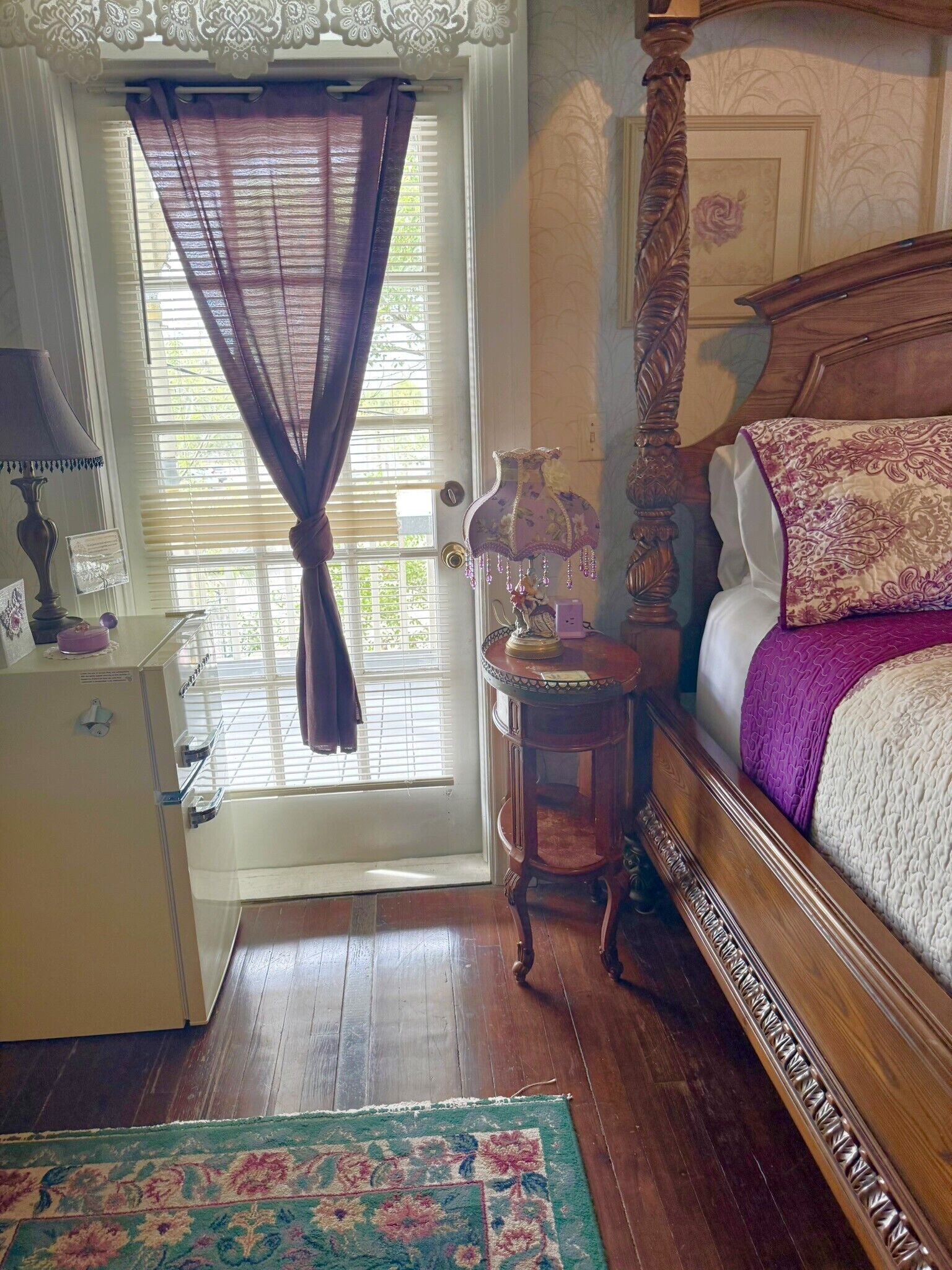 Une chambre à coucher avec un lit en bois, une table de chevet, une commode, une fenêtre avec des rideaux et un tapis.