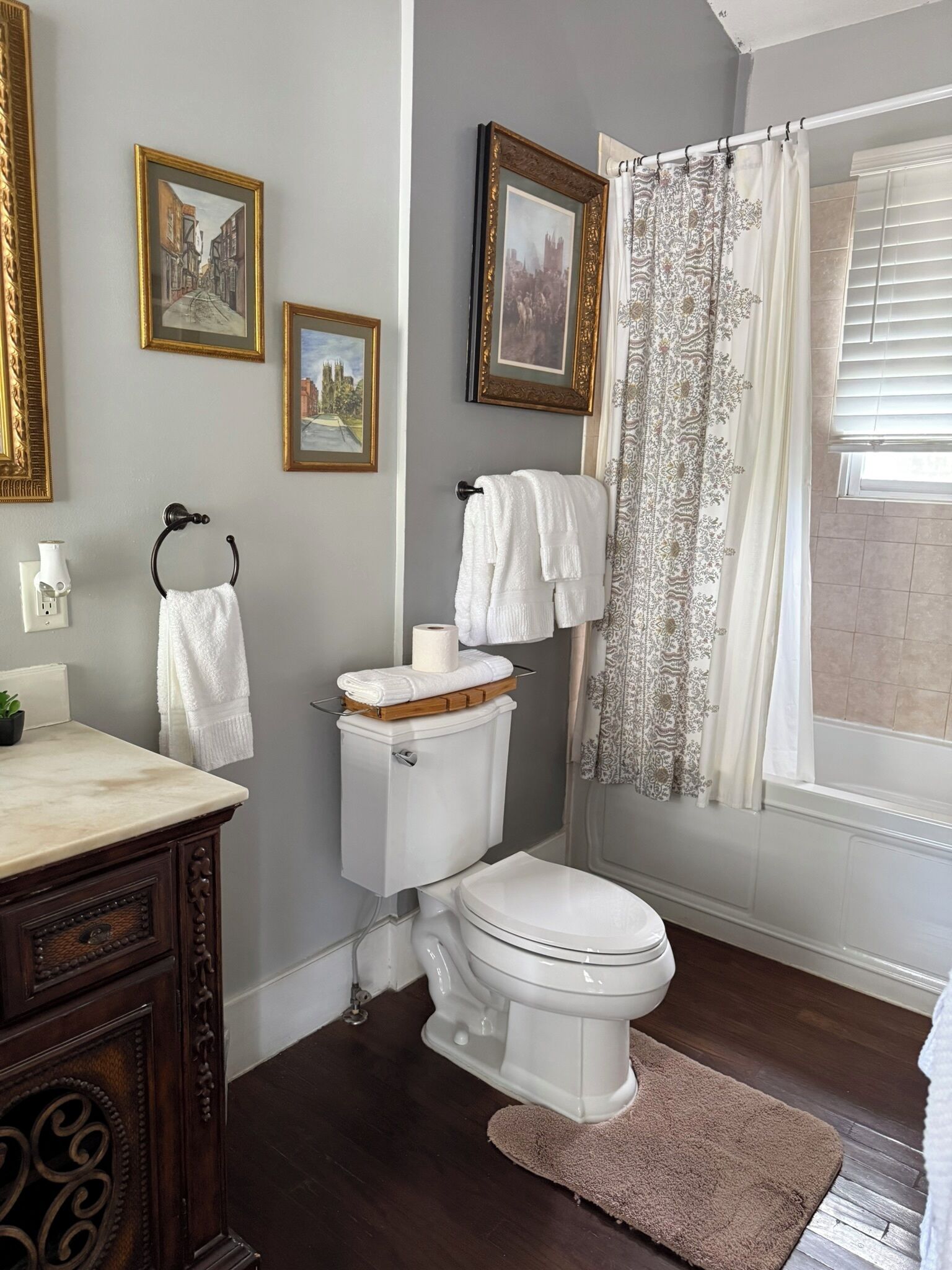 A bathroom with a toilet, a sink, a mirror, framed pictures on the wall, and a shower curtain.