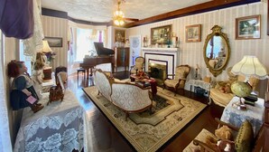 A vintage-style living room with a grand piano, a fireplace, and classic furniture. - Penny Farthing Inn (St. Augustine)
