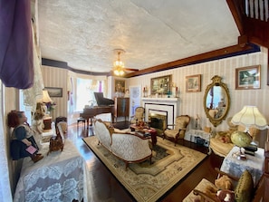 A vintage-style living room with a grand piano, a fireplace, and classic furniture. - Penny Farthing Inn (St. Augustine)