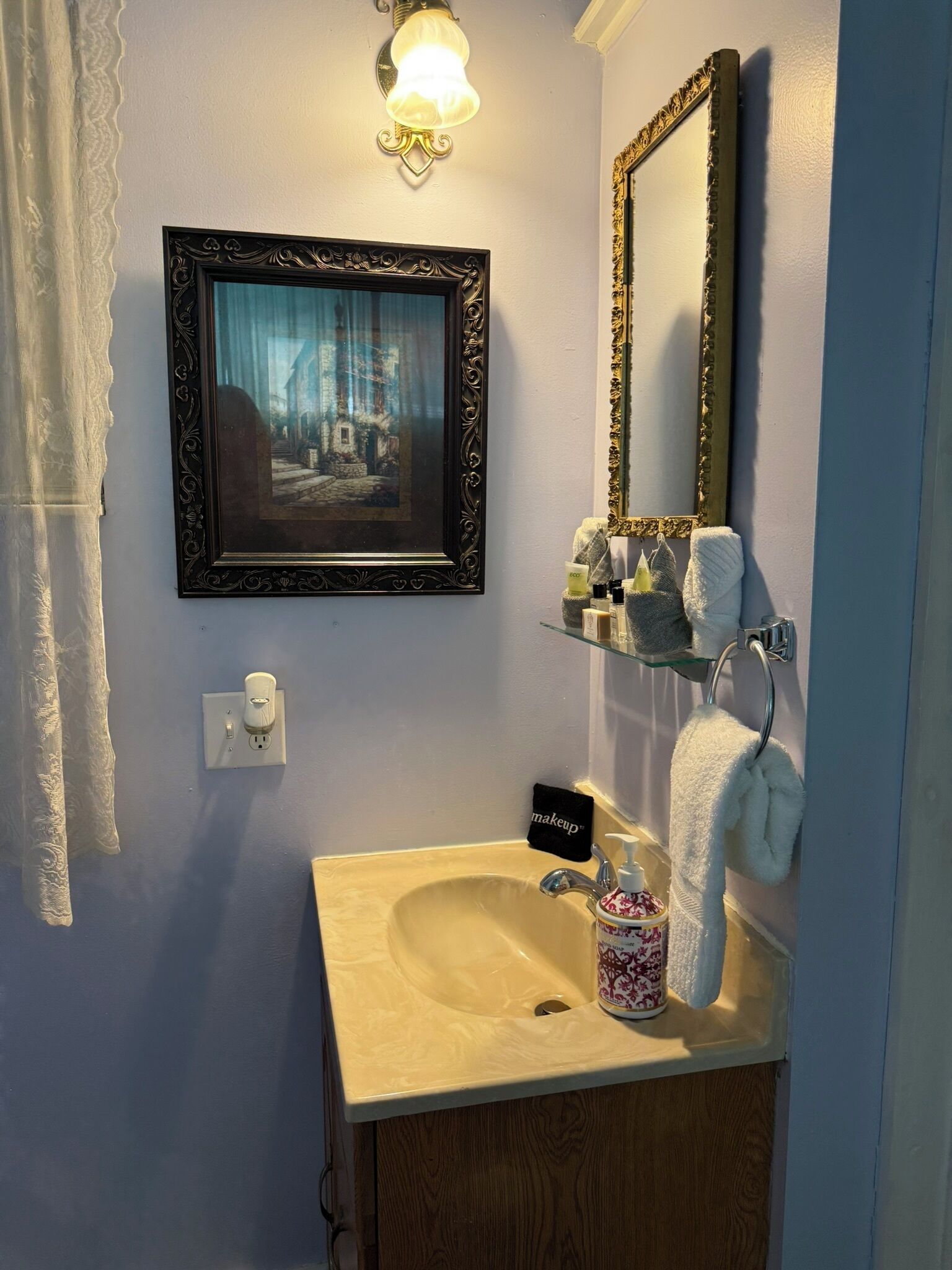 A bathroom with a sink, mirror, framed picture, and toiletries.