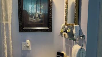 A bathroom with a sink, mirror, framed picture, and toiletries.