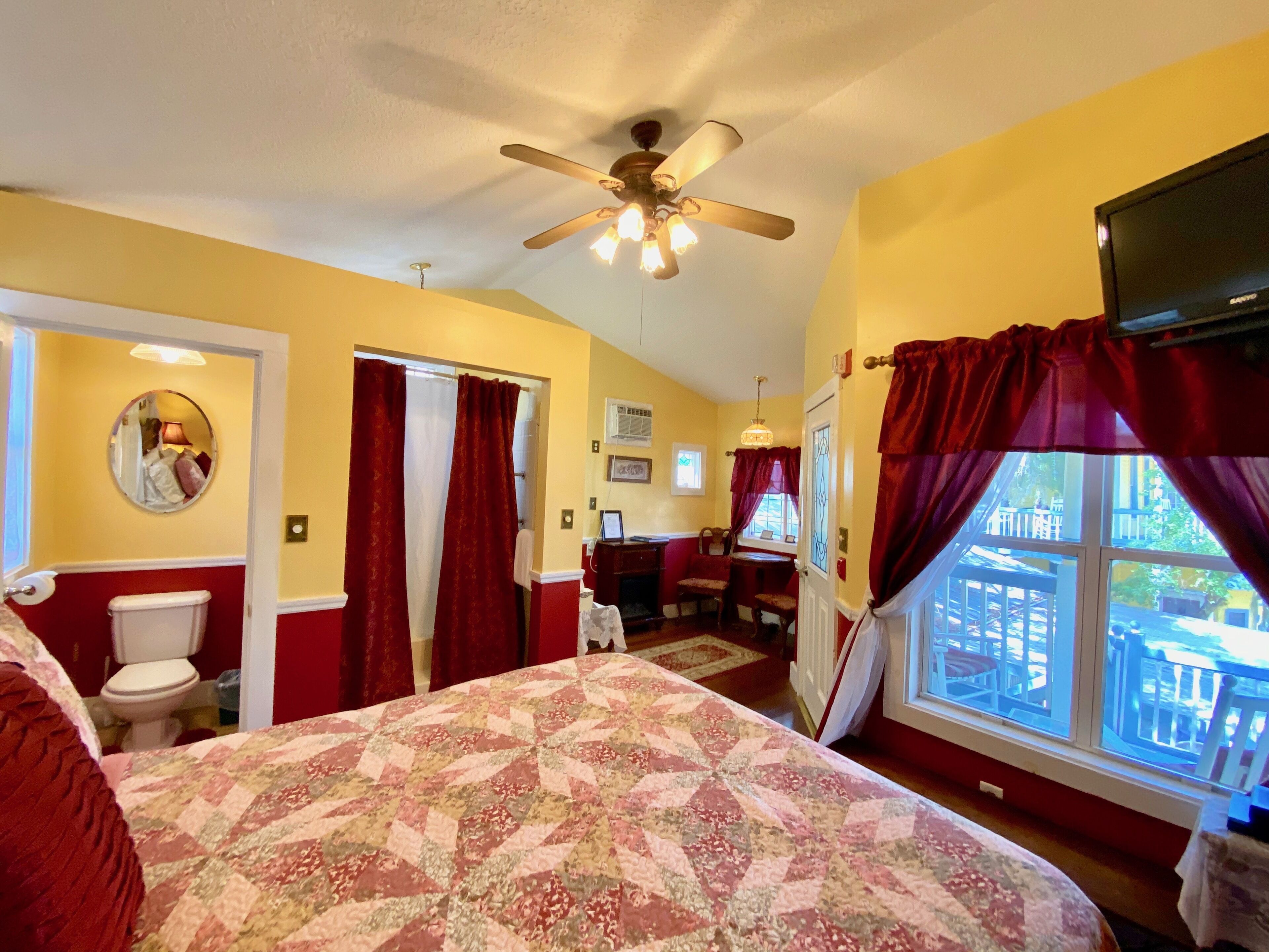 A bedroom with a bed, a ceiling fan, a window with curtains, a desk, and a chair.