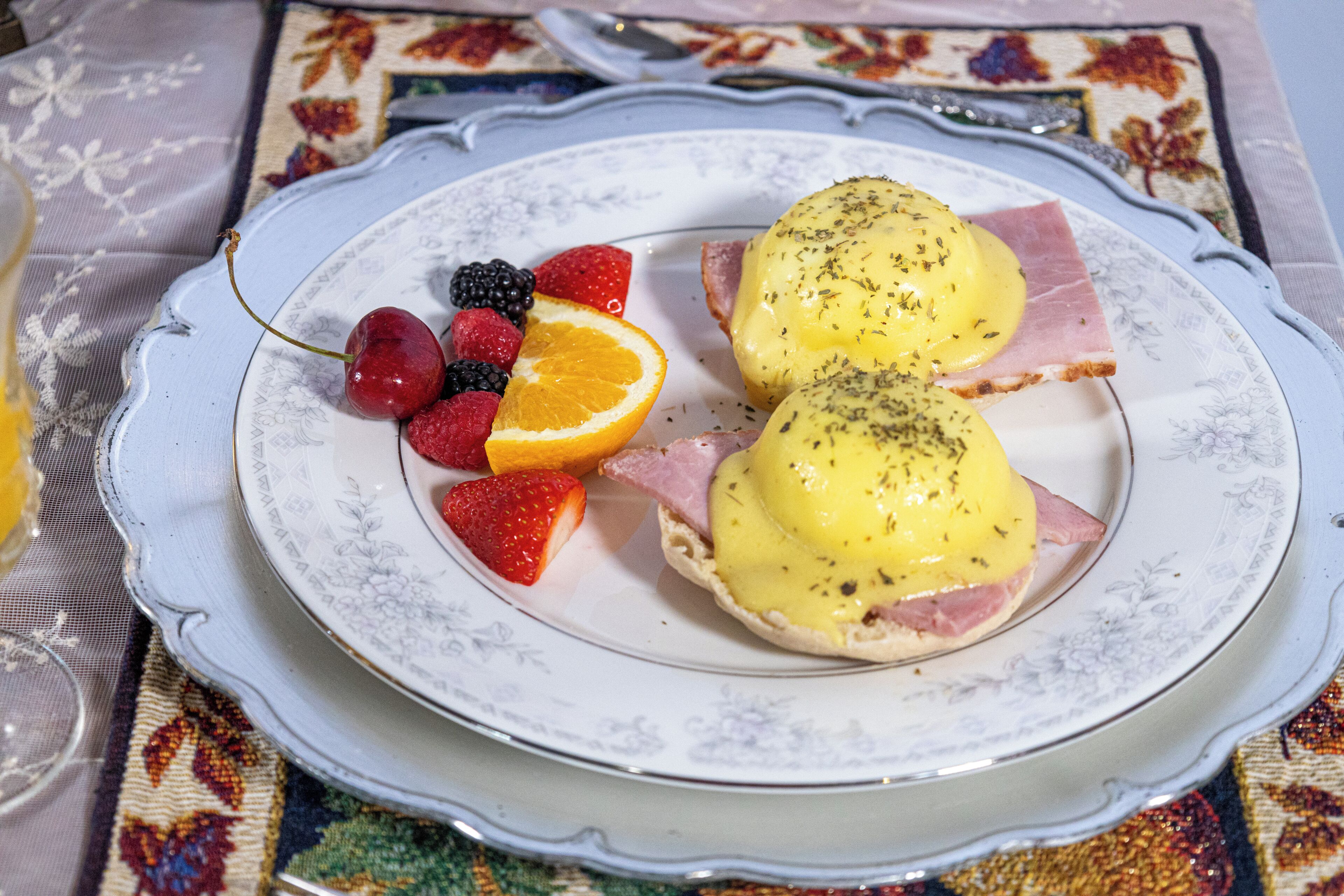 A plate with eggs benedict, strawberries, blackberries, and an orange slice.