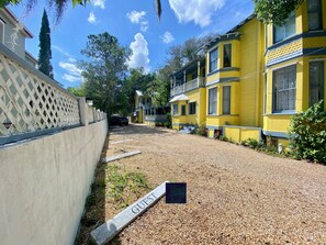 A gravel driveway leading to a yellow building with a guest sign. - Penny Farthing Inn (St. Augustine)
