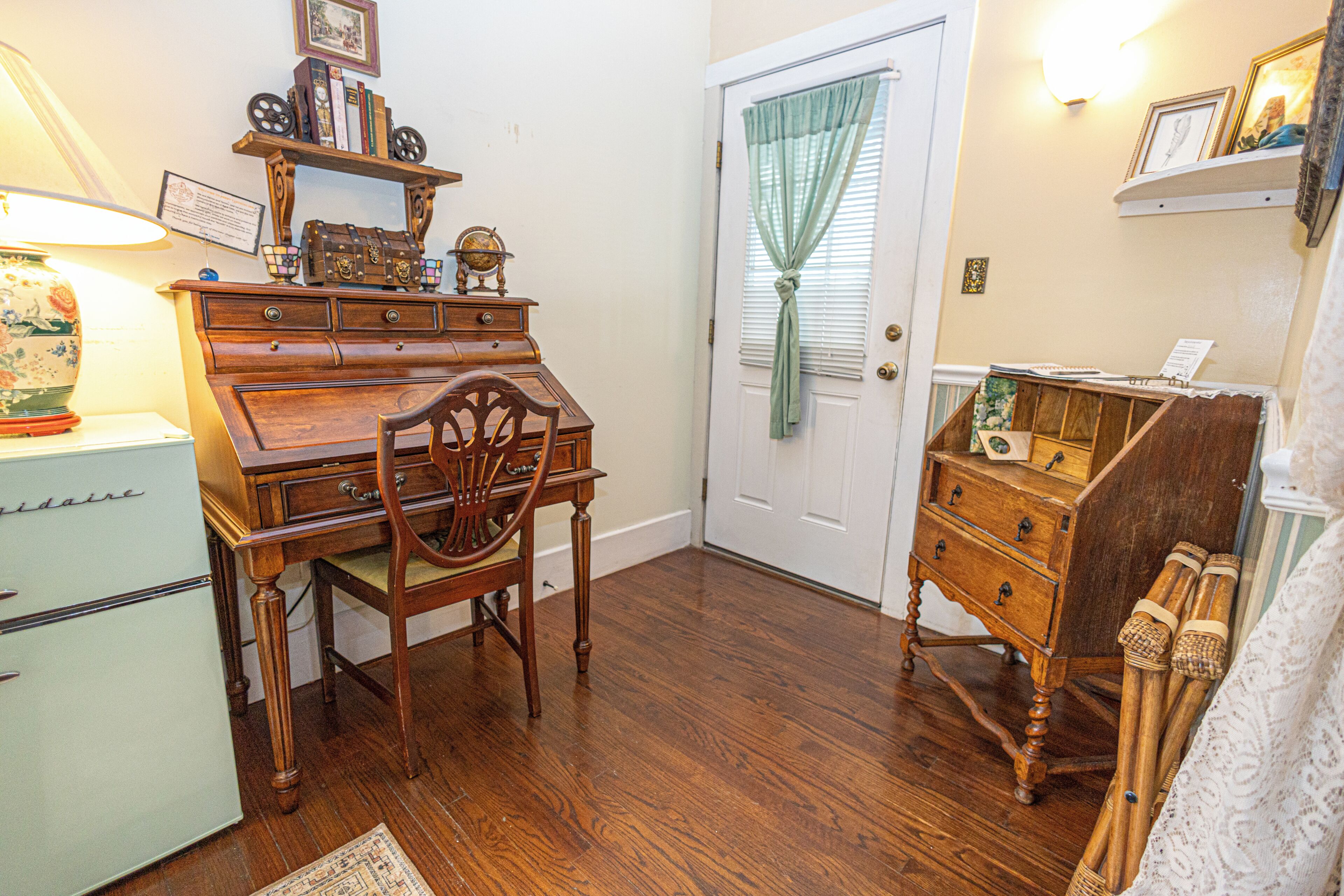A room with a wooden desk, chair, and a dresser with drawers.